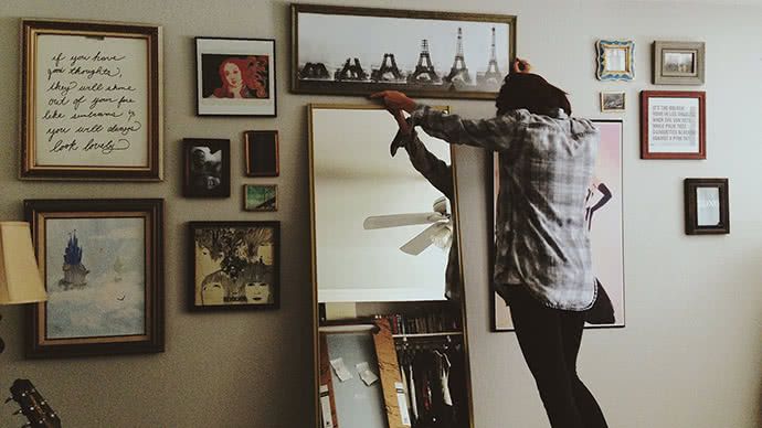 A woman hanging artwork on a wall.