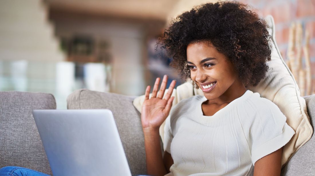 woman smiling and waving while video chatting on laptop