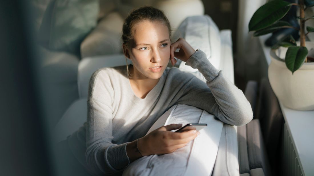 woman sitting on couch holding phone while gazing out the window