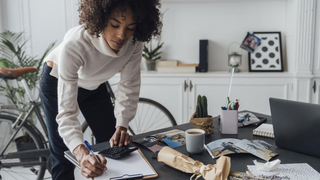 freelancer using calculator and taking notes at desk