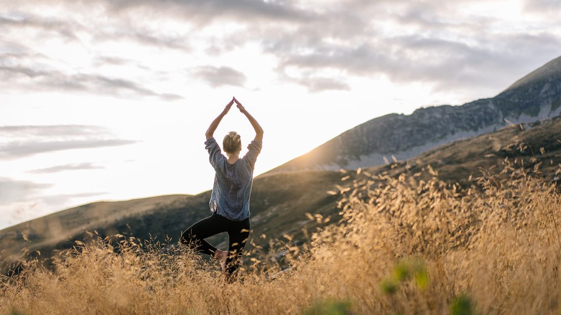 Woman doing yoga in the mountains while thinking about financial wellness.