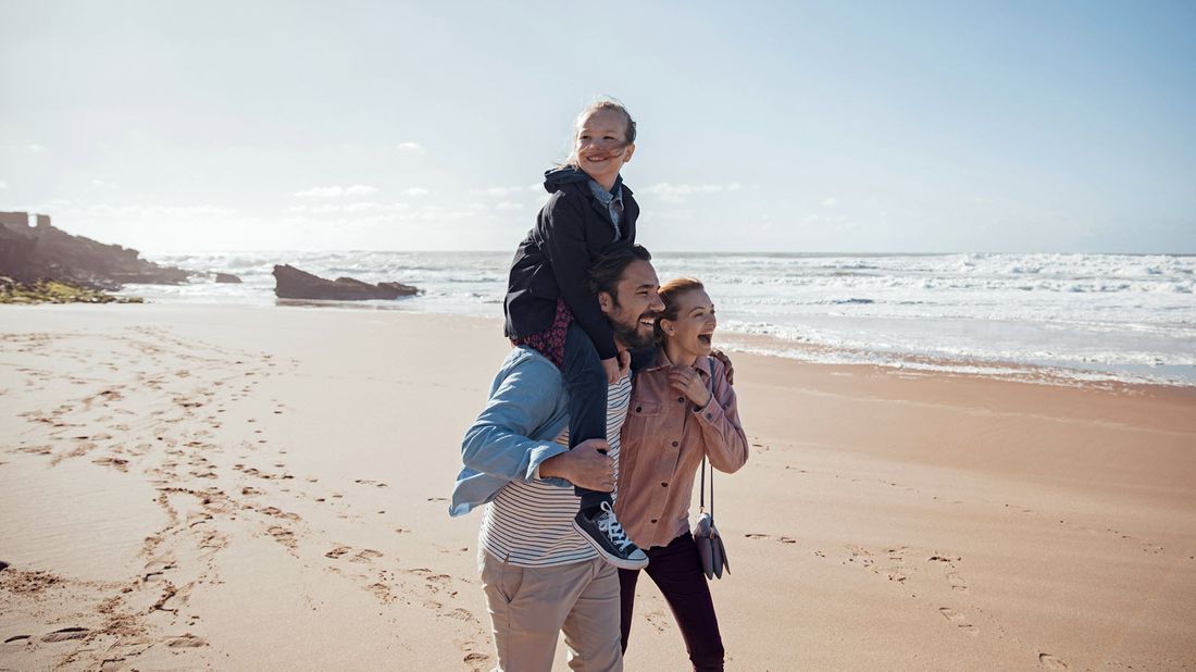 Couple walking on the beach with their daughter after learning how whole life insurance works.