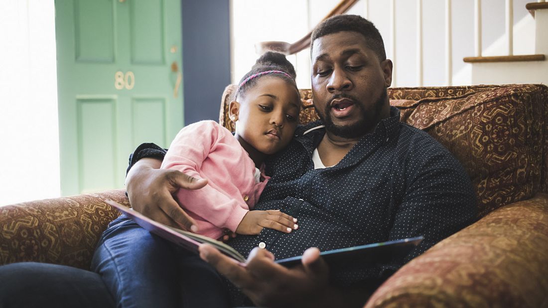 A man reading a book to his daughter 