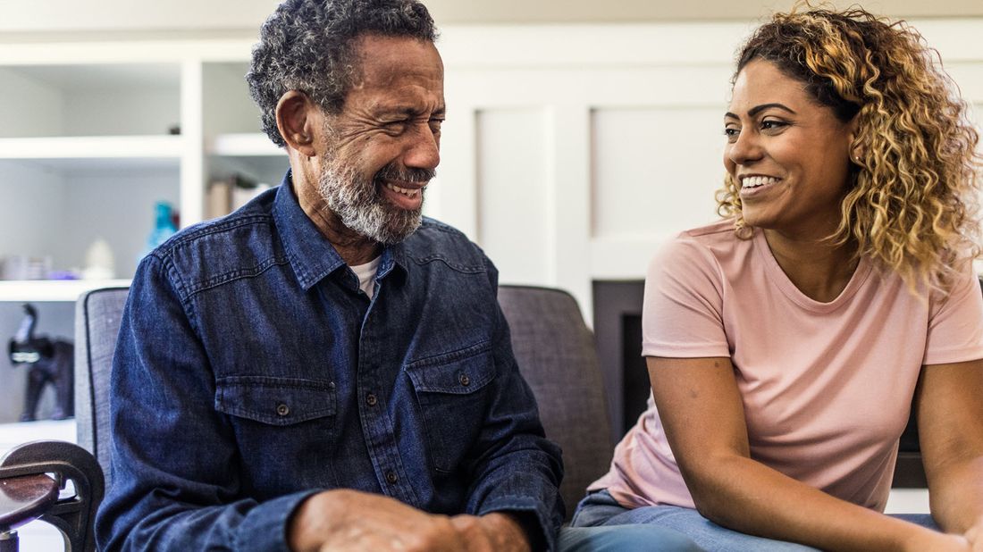 An elderly father and his daughter talk to eachother on the couch