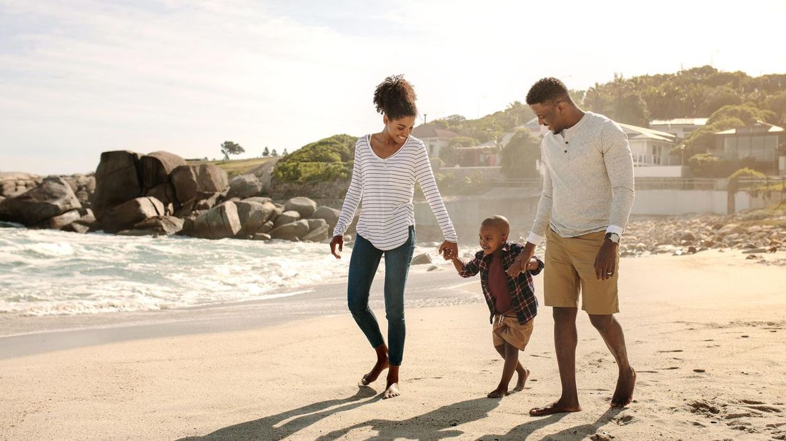 Family who has done financial planning walking on beach with young child.