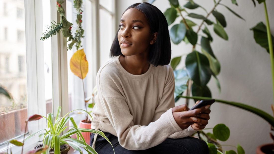 Young woman sitting by window with smartphone wondering about cost of term life insurance 