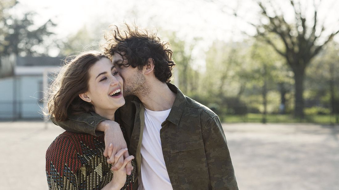 Man with his arm around woman kissing her on the cheek.