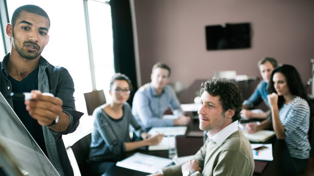 Man writing long-term business goals on board in conference room full of coworkers