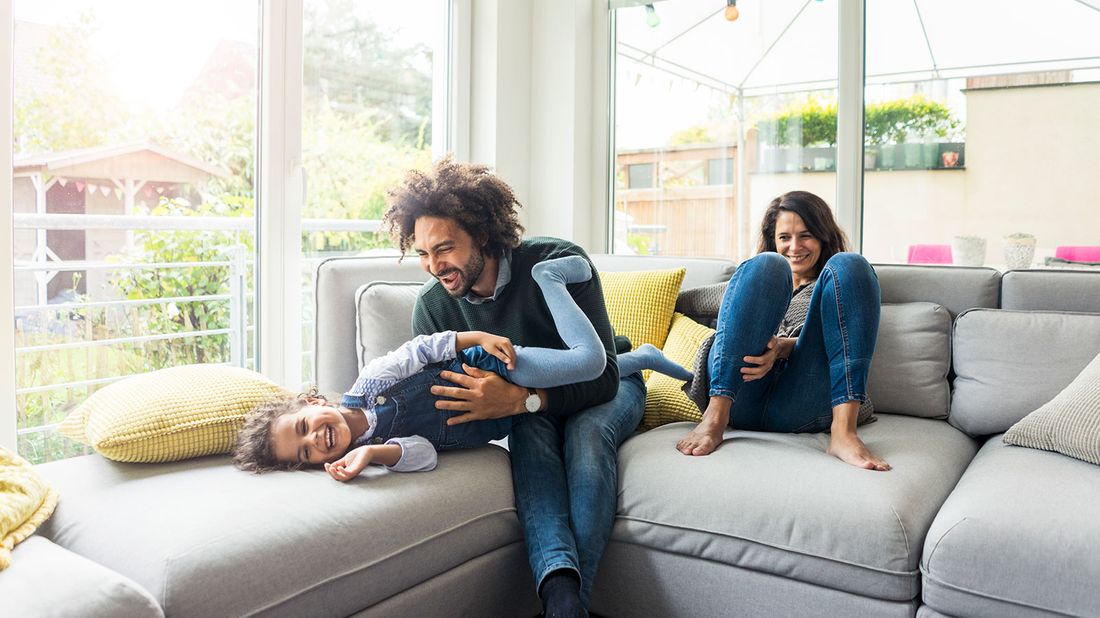 Dad playing with daughter on their couch in the living room after buying a second home