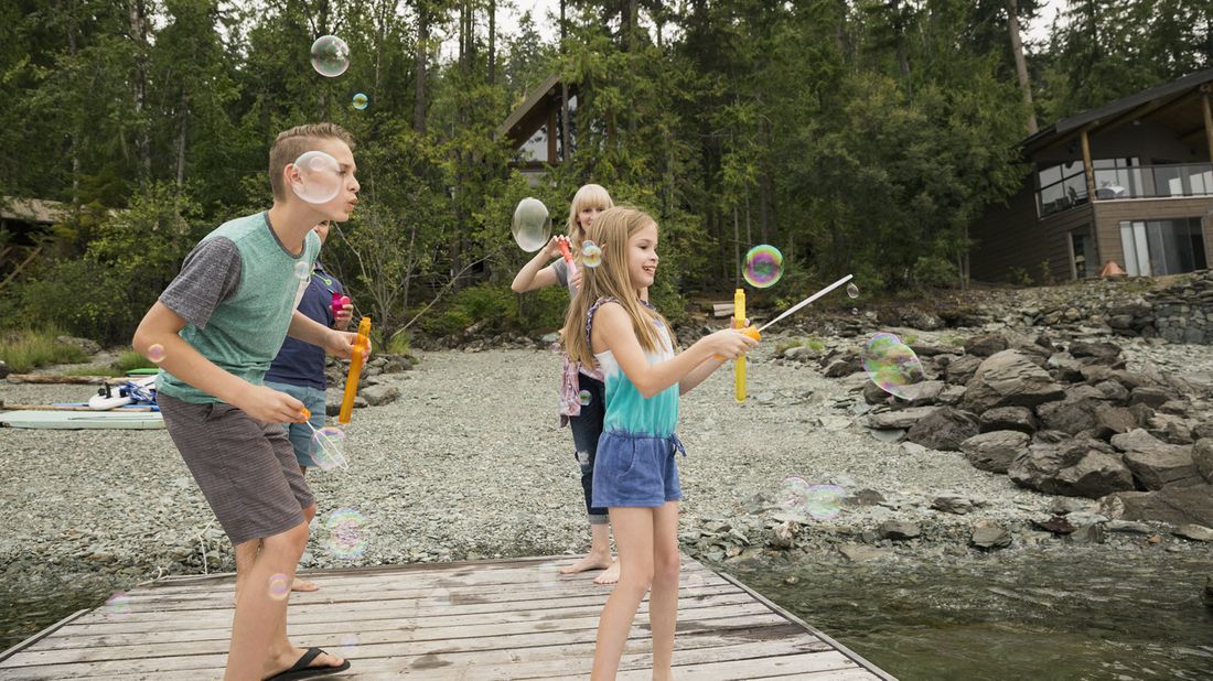 Family blowing bubbles on the dock at a vacation home shared with other families.