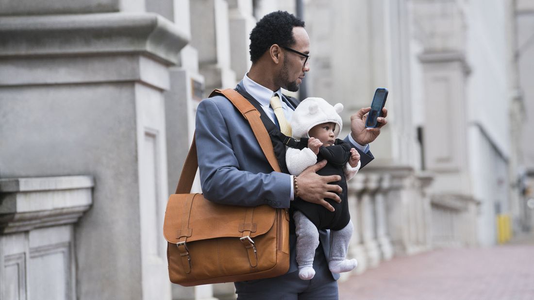 A business man checking his phone while holding a baby