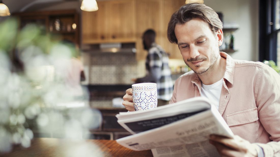 A man reading the newspaper and drinking coffee