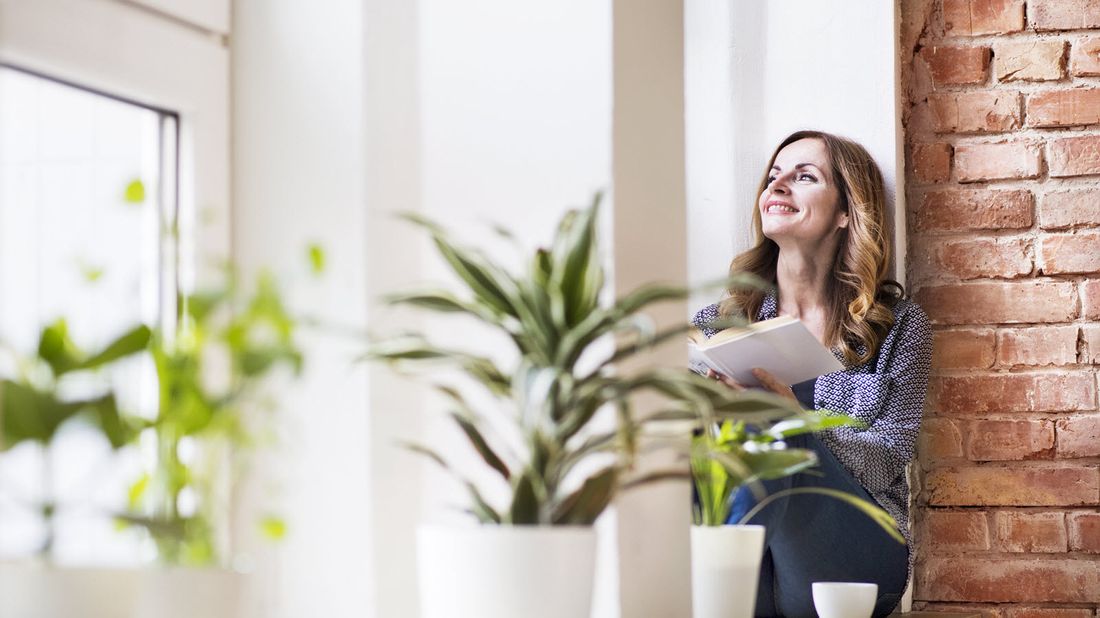 Woman on window ledge reading a book thinking about the questions to ask before buying an annuity.