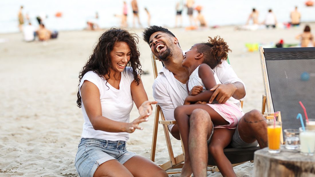 mother, father and daughter laughing on beach 