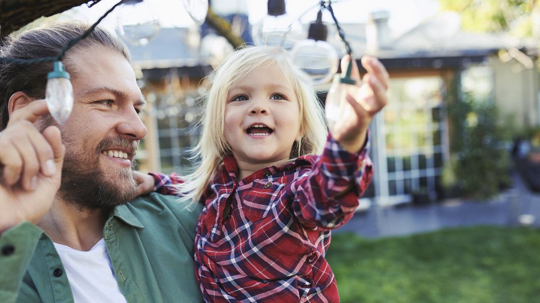 Dad playing with a string of lights with his daughter as he thinks about how life insurance works.