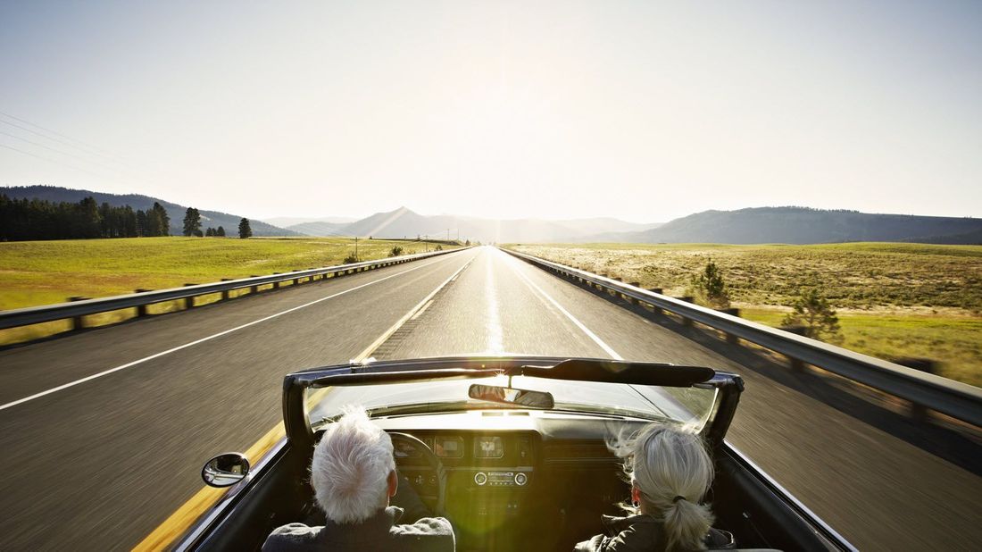 A retired couple driving a convertible on the highway