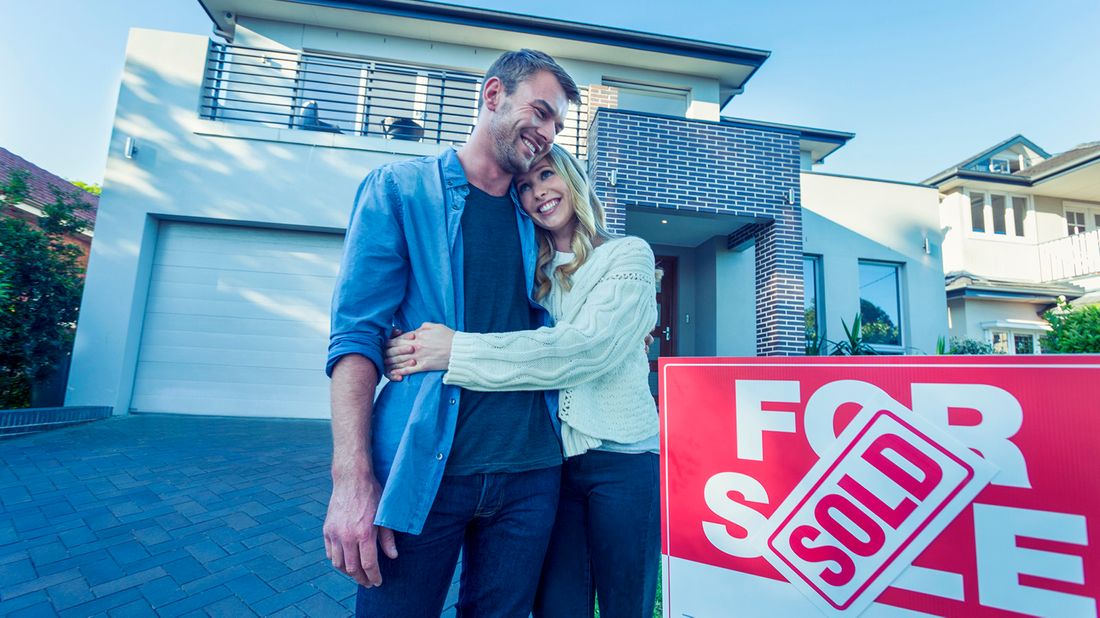 Couple standing in front of a home with for-sale sign.