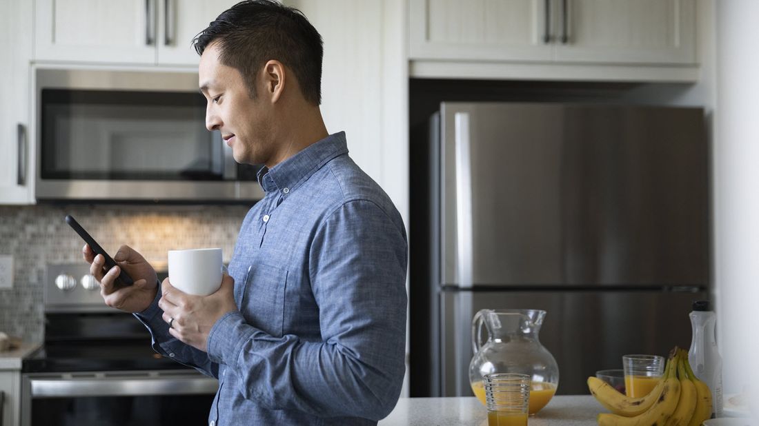 Man drinking coffee and looking at his phone as he does a year-end financial wellness checkup.