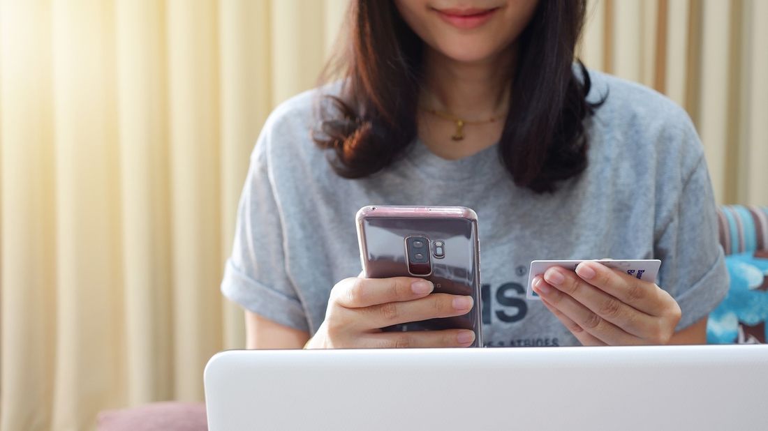 Woman holding mobile phone with credit card pondering credit report and score.