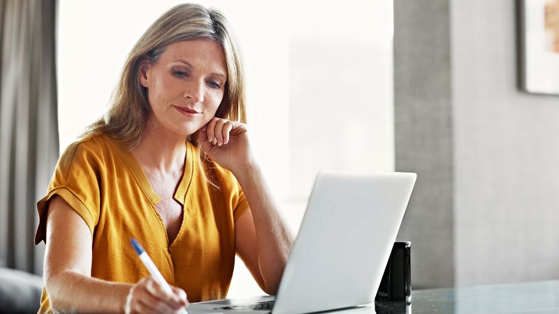 Woman with laptop and notebook prepping financially for a job loss.