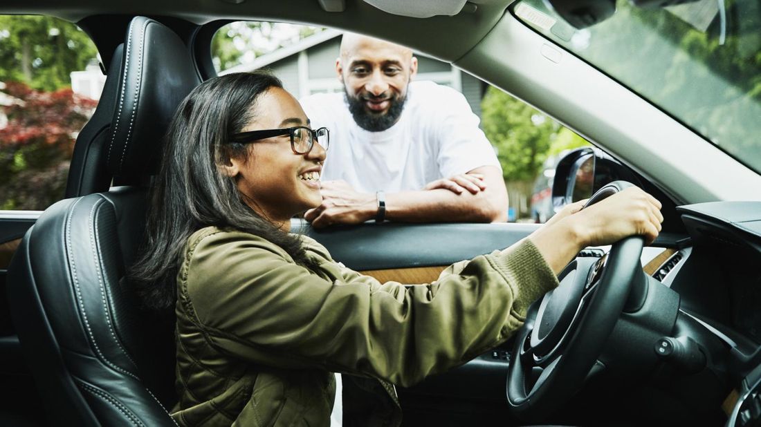 Father leaning in car window instructing daughter in driver’s seat