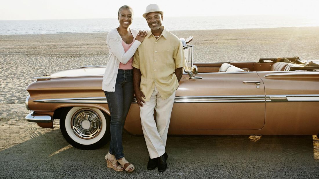 Couple standing next to convertible on beach