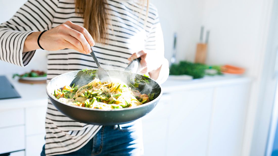 Young woman holding pan with vegan pasta dish