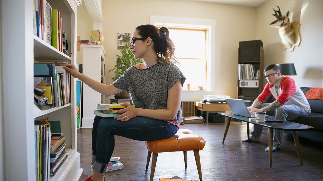 woman tidying bookshelves in living room