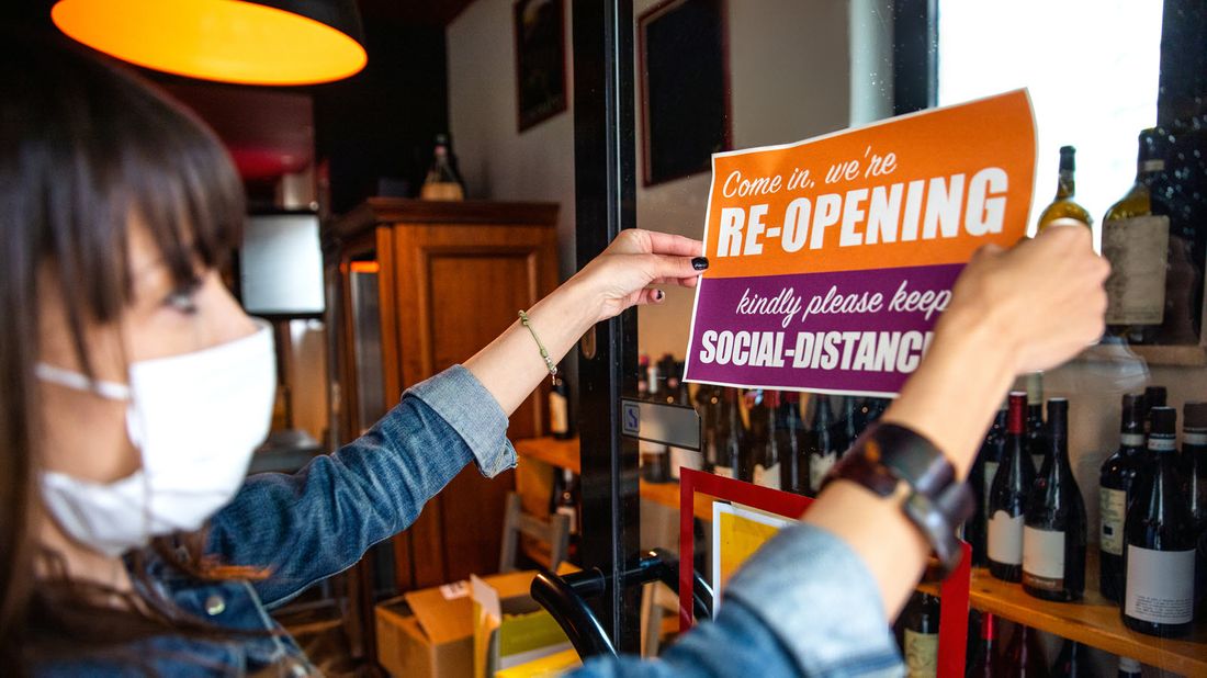 A shop owner displays an open sign with social distancing recommendations