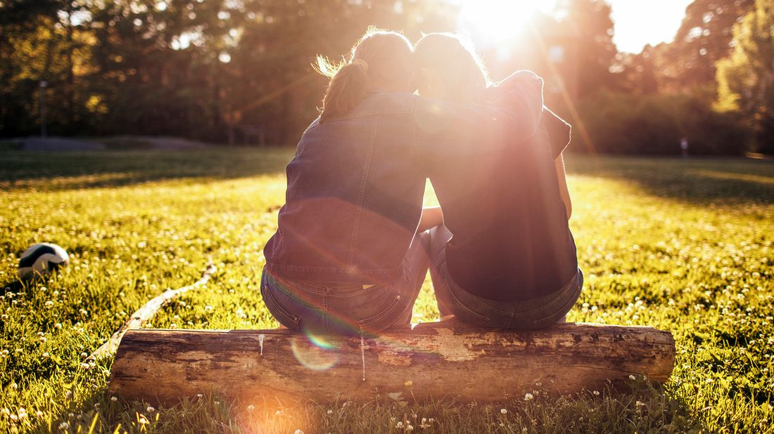 Two women sitting on a log in sunlight. 