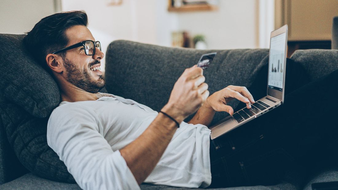 Man laying on a couch making an online purchase.