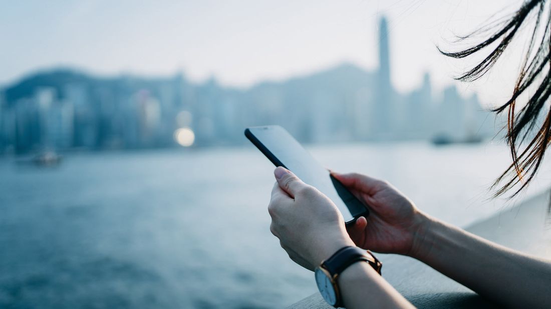 Woman looking at phone along a river in a city.