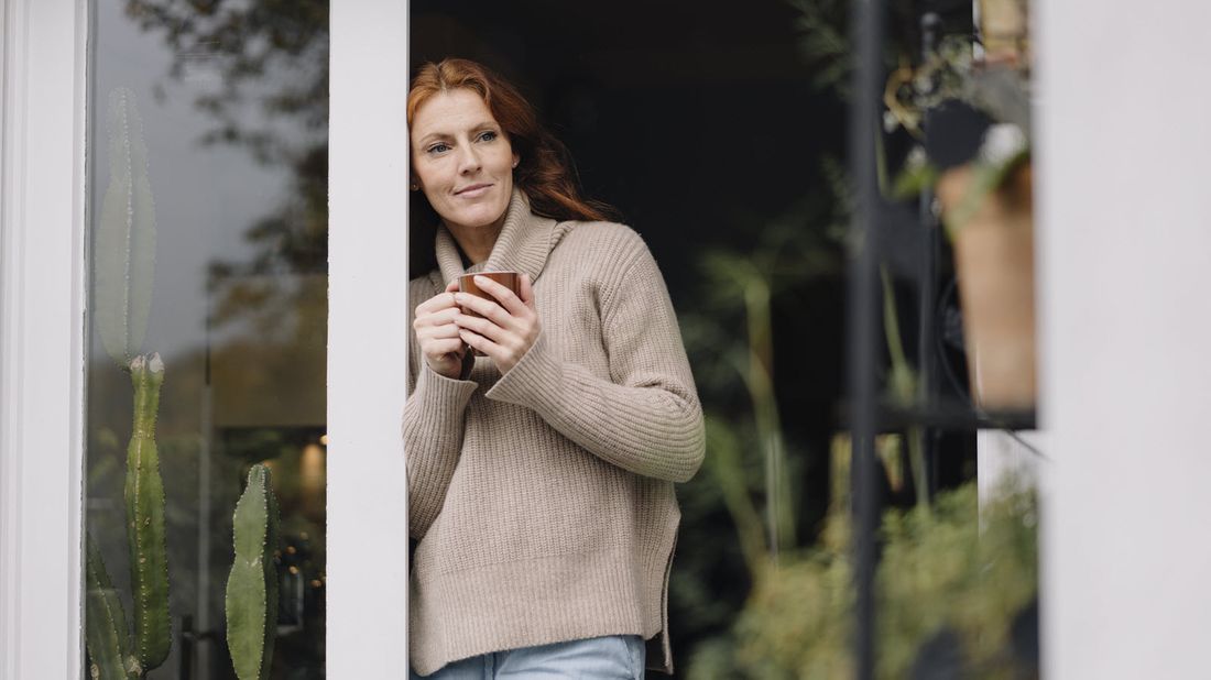 Woman standing at door with coffee mug.