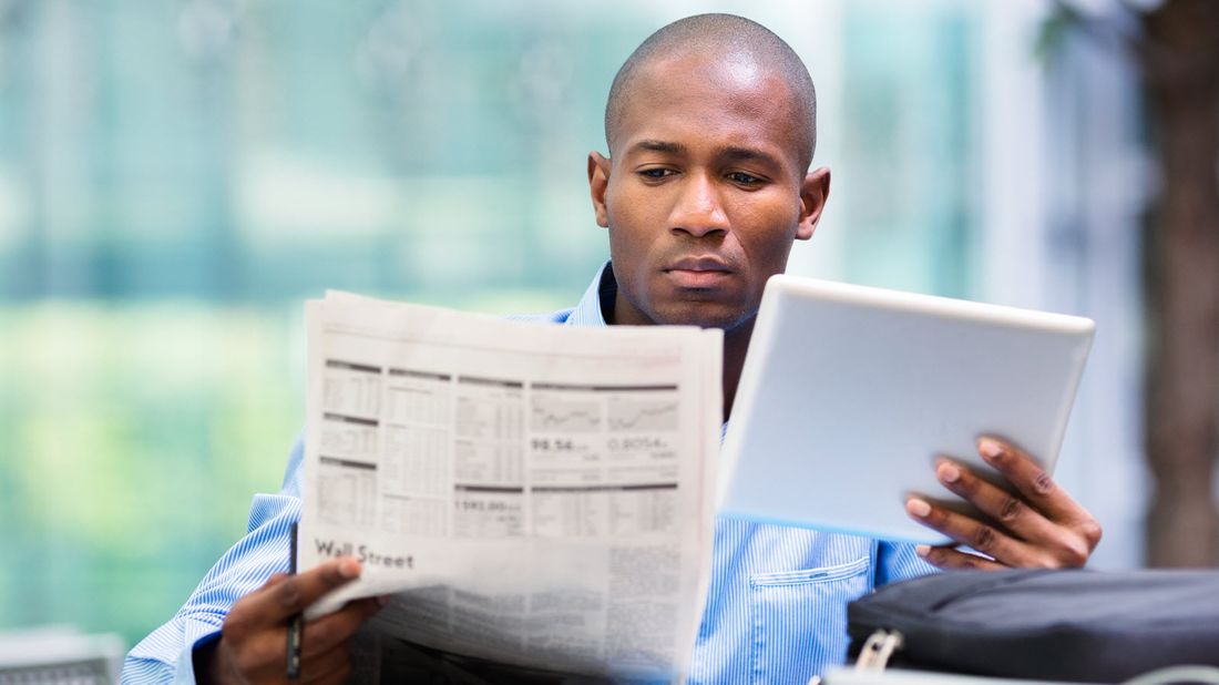 Man looking at stock market news in a newspaper and on a tablet.