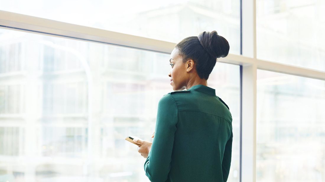 Woman looking out building window while reading Northwestern Mutual Market Commentary.