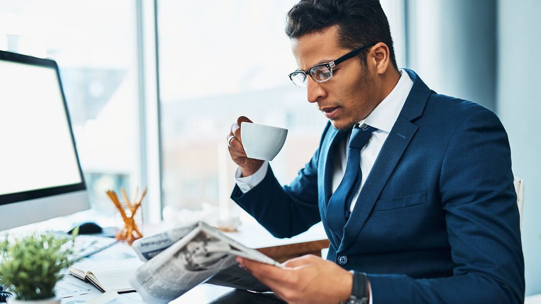 Man at desk drinking coffee and reading Northwestern Mutual Market Commentary.