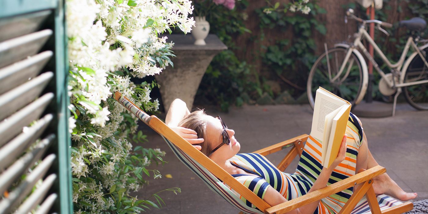 woman relaxing on deck chair in backyard reading