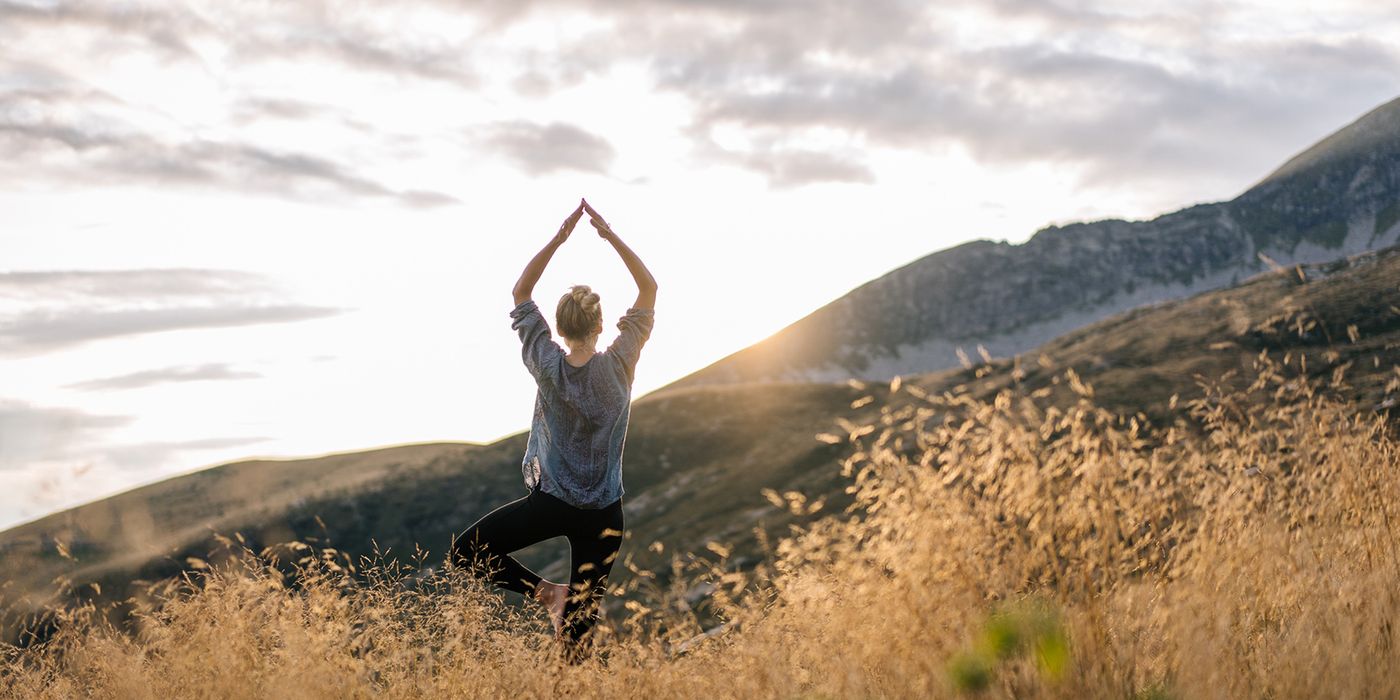 Woman doing yoga in the mountains while thinking about financial wellness.