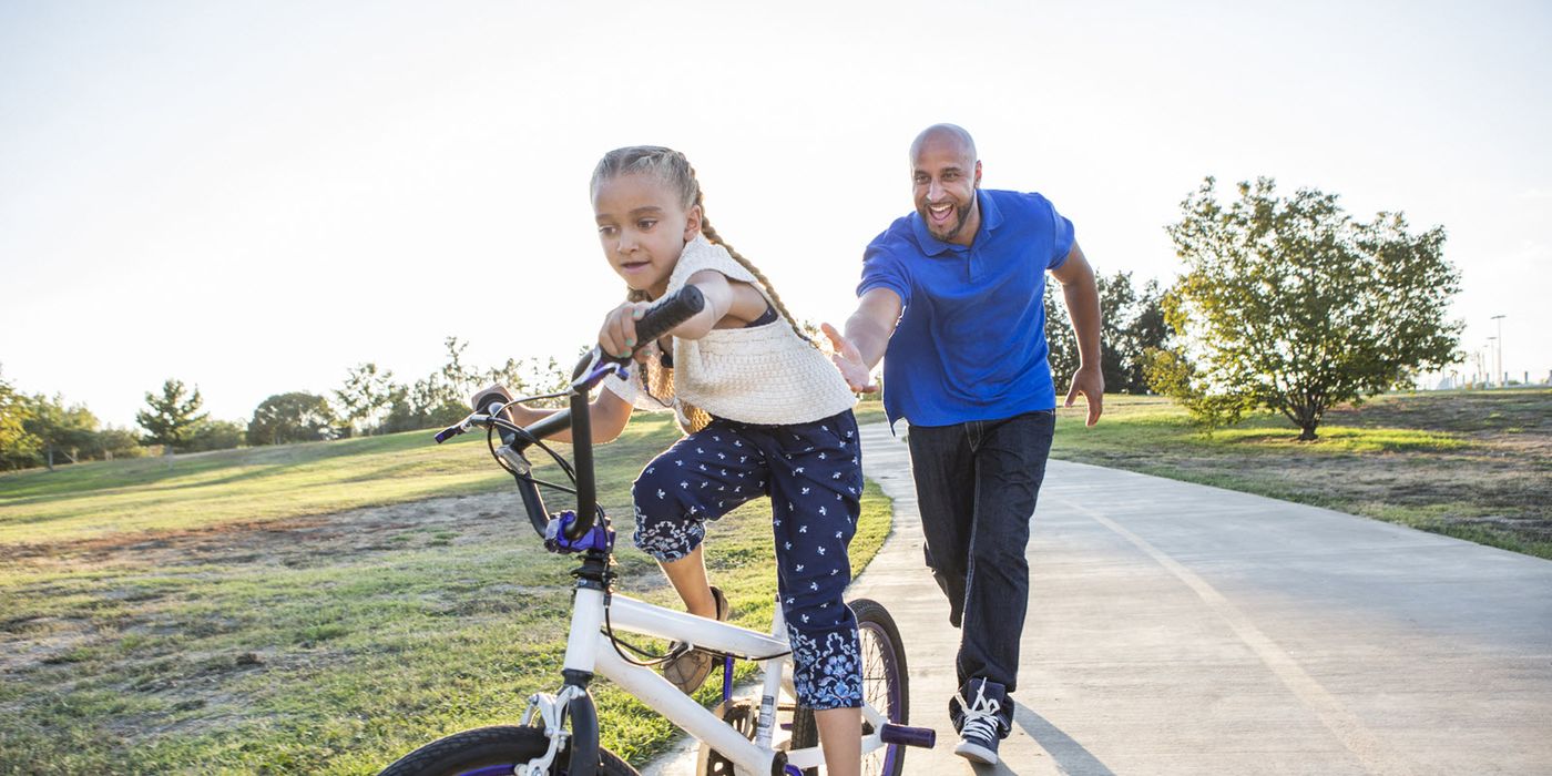 Dad teaching his daughter to ride a bike.