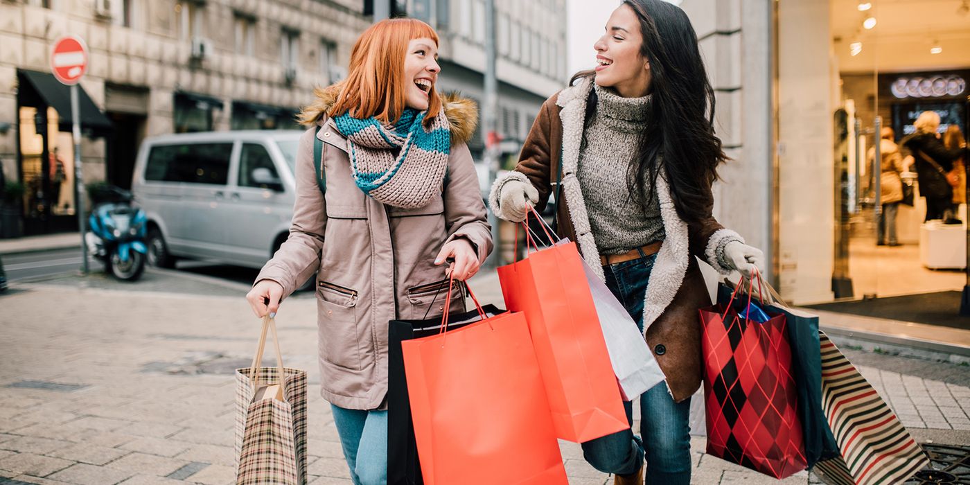 Two women carrying shopping bags trying to prevent holiday overspending.