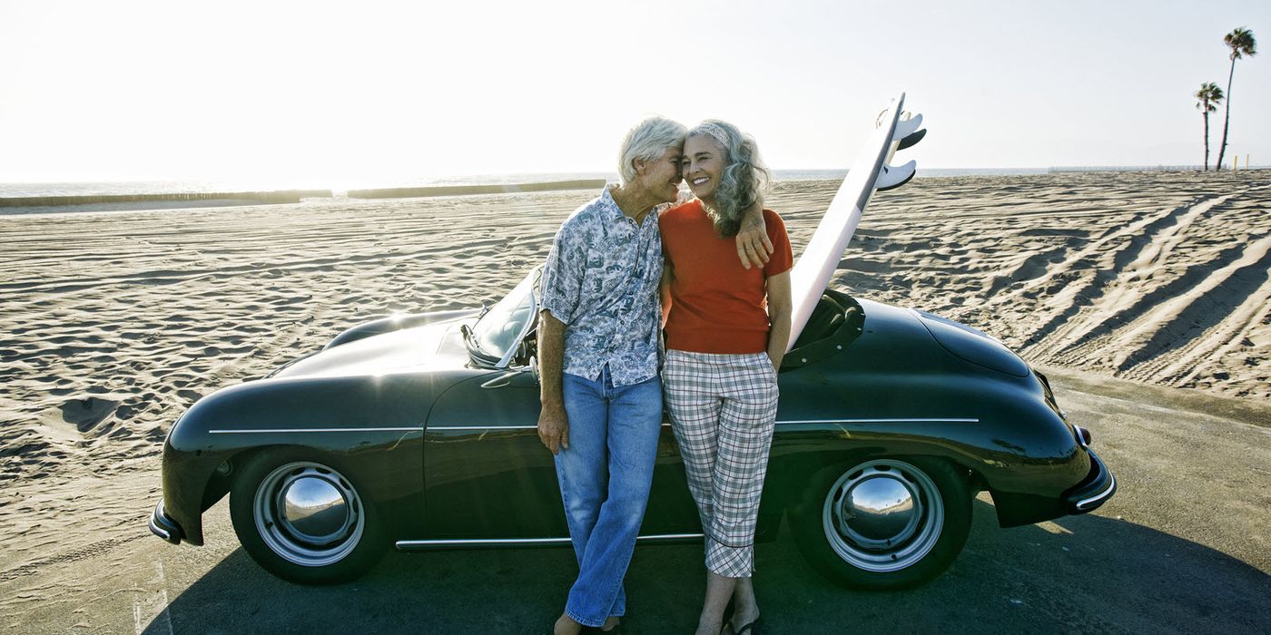 Retired couple posing in front of a car at the beach.