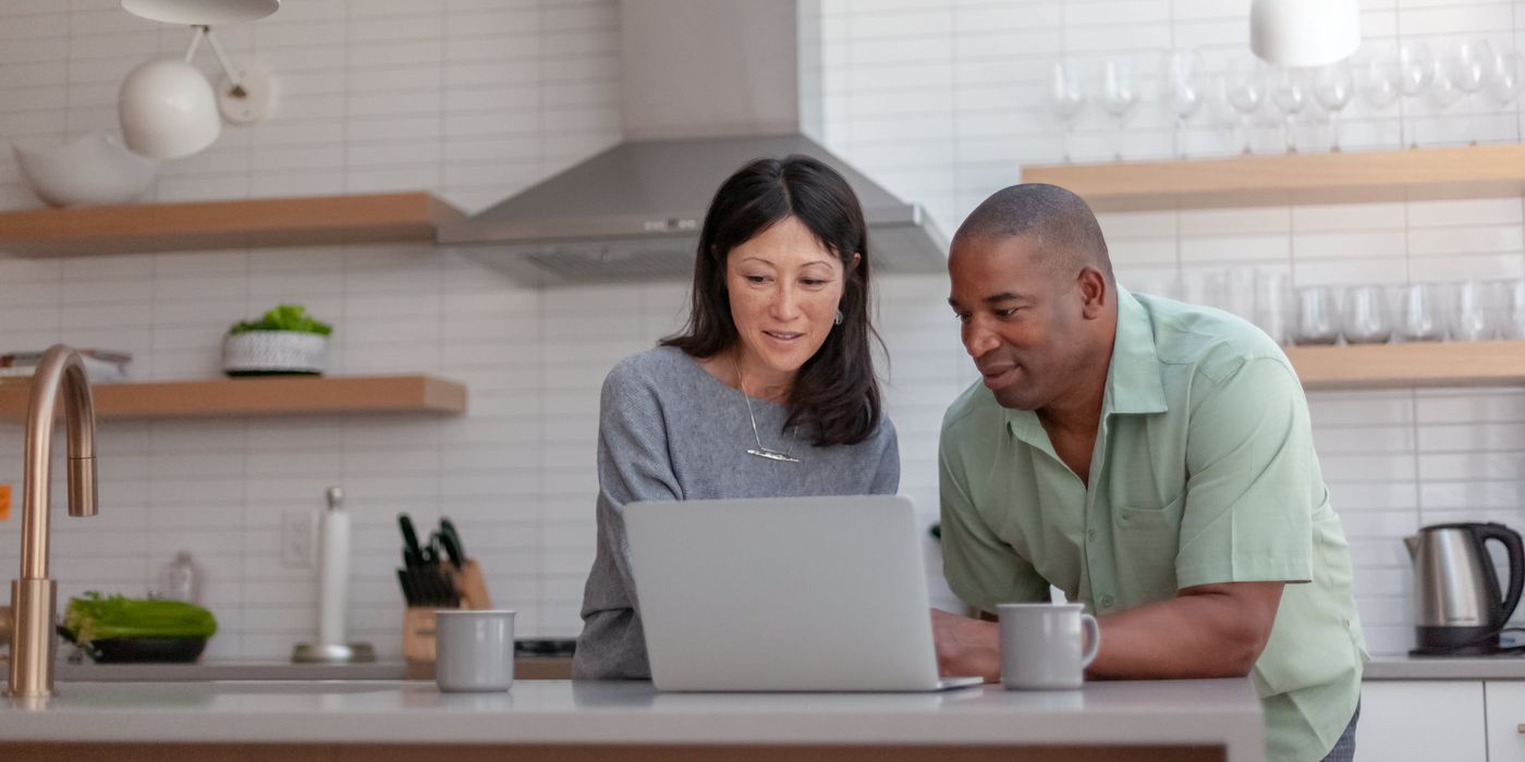 Husband and wife looking at a computer while standing in their kitchen thinking about smart moves for rising interest rates