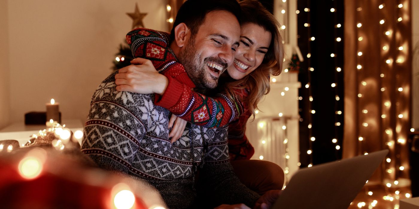 Couple in Christmas sweaters on a couch looking at a laptop learning how to improve their finances in December