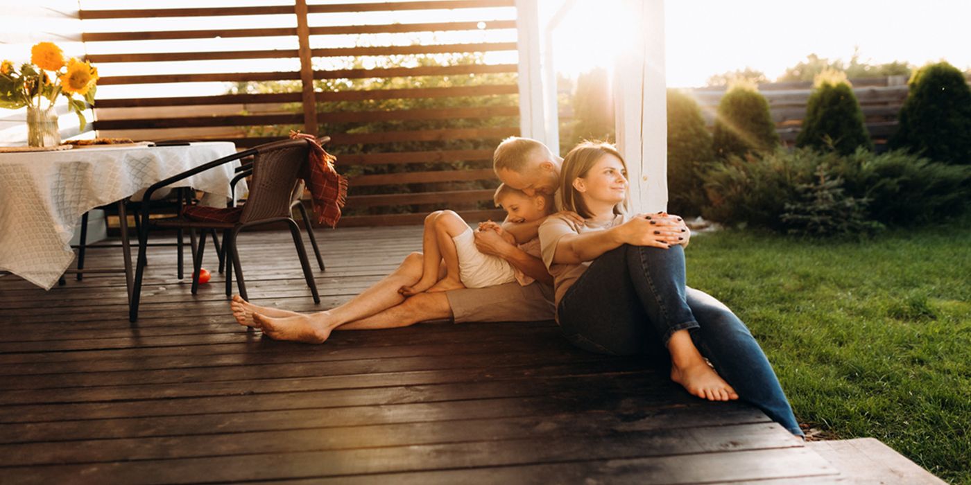 two parents with their young child sitting outside on the porch enjoying the sunset