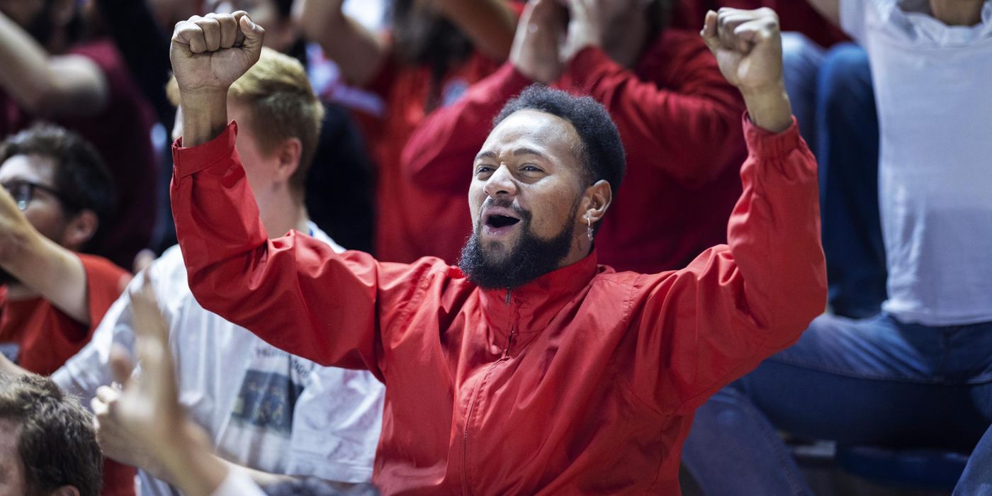 Adult male soccer fan passionately cheers and raises his arms while standing in a large crowd of supporters