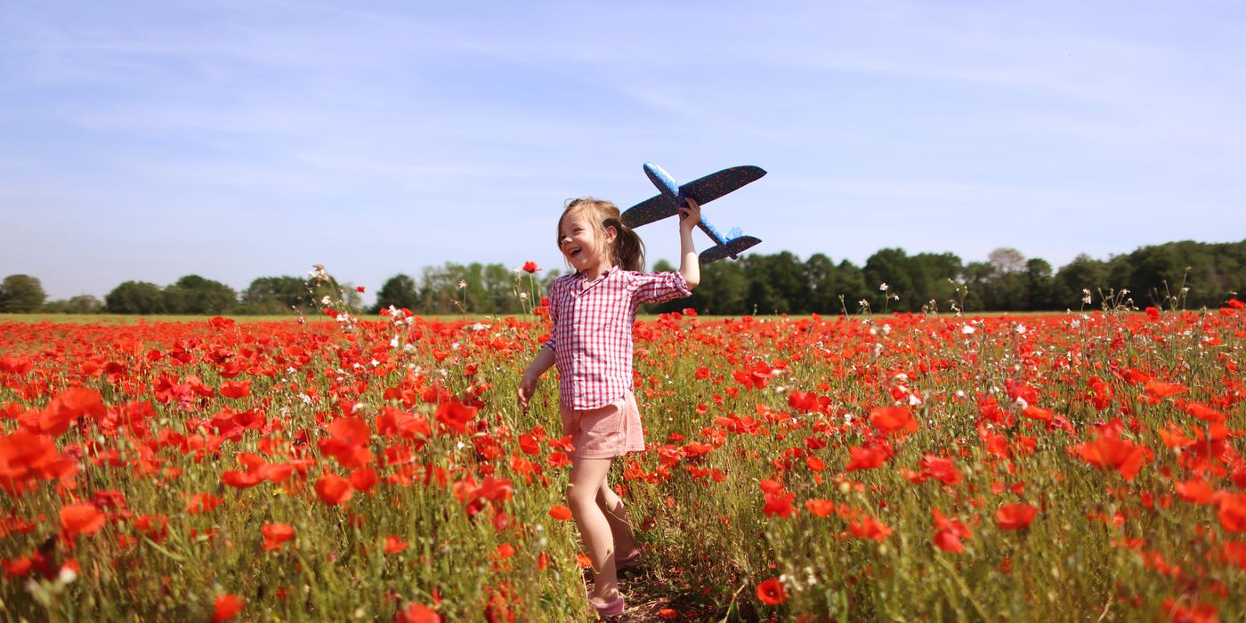 A girl playing with a plane in a field of flowers