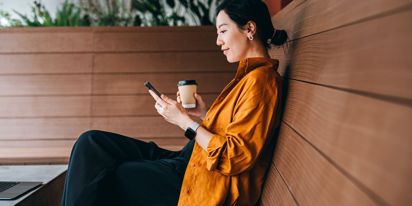 Young woman sitting in a sidewalk cafe with a cup of coffee and using her smartphone.