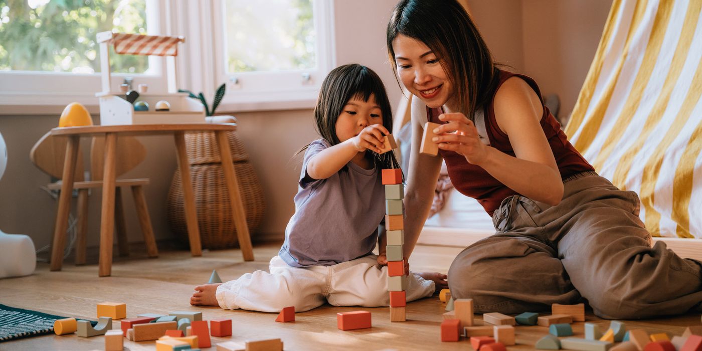 Mother and her daughter having fun, playing with toys together in the bedroom.