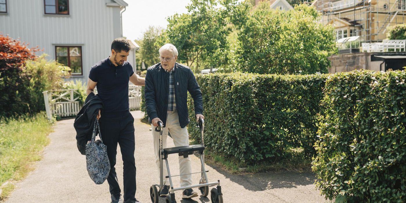 Male caregiver walking with senior man using rollator in park at sunny day
