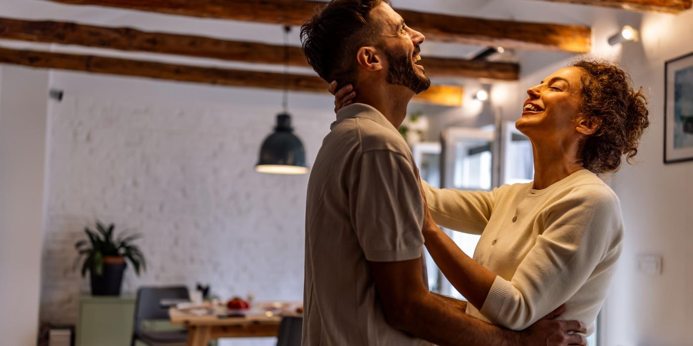 joyful couple shares a warm hug and big smile in a bright, cozy living space, conveying love, connection, and positive energy in a home environment.